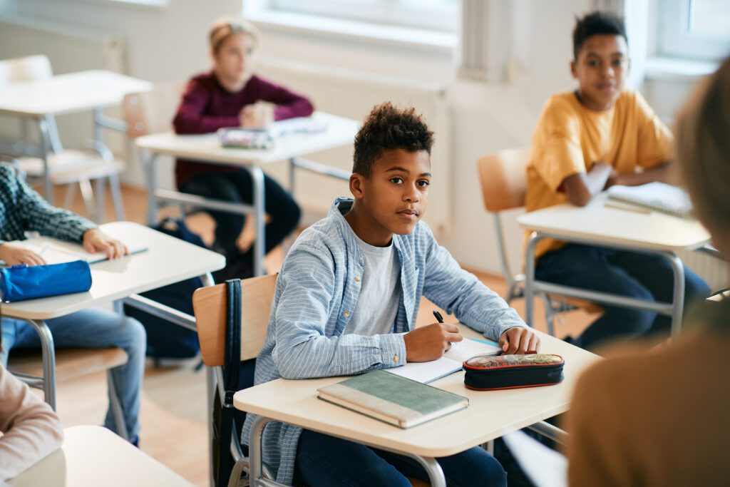 Black schoolboy paying attention and taking notes on sentence skills during a class at elementary school.